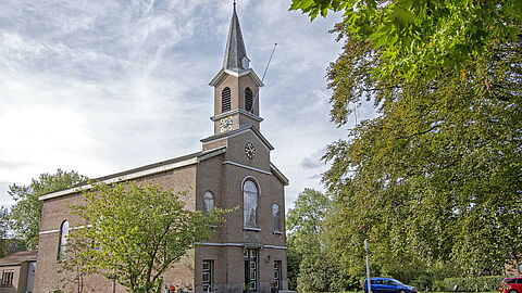 Dorpskerk in Hekelingen. Gebouw van baksteen met kleine ramen en kleine toren met spits.