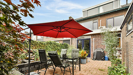 Achtertuin met tuinset en parasol van rijwoning aan de Tollensstraat 3 in Spijkenisse.