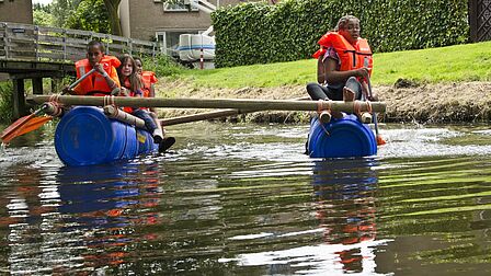 Kinderen op een zelfgemaakt vlot op het water in De Hoek in Spijkenisse.
