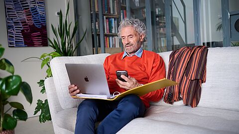 Oudere meneer met laptop op schoot.