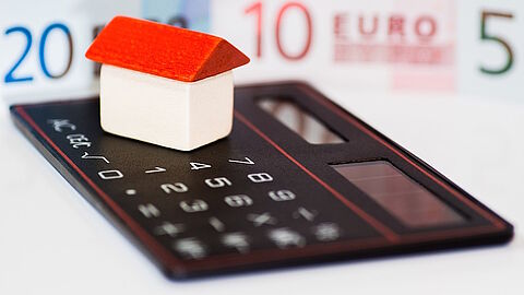 Speelgoedhuisje op rekenmachine met eurobiljetten eromheen.