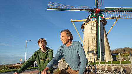 Fietsers fietsen langs de molen van Nieuwenhoorn.